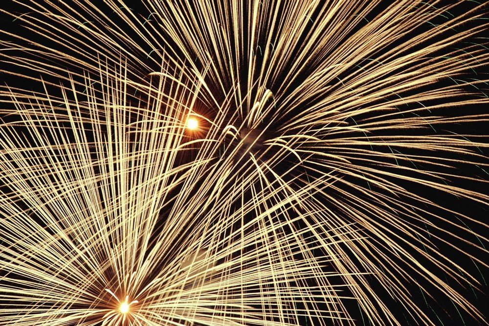 Golden fireworks bursting with radiating trails and bright starburst centers against a black night sky.