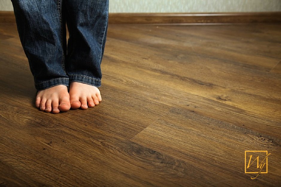 Bare feet standing on a warm-toned wood-look floor installed over a concealed electric radiant floor heating system.