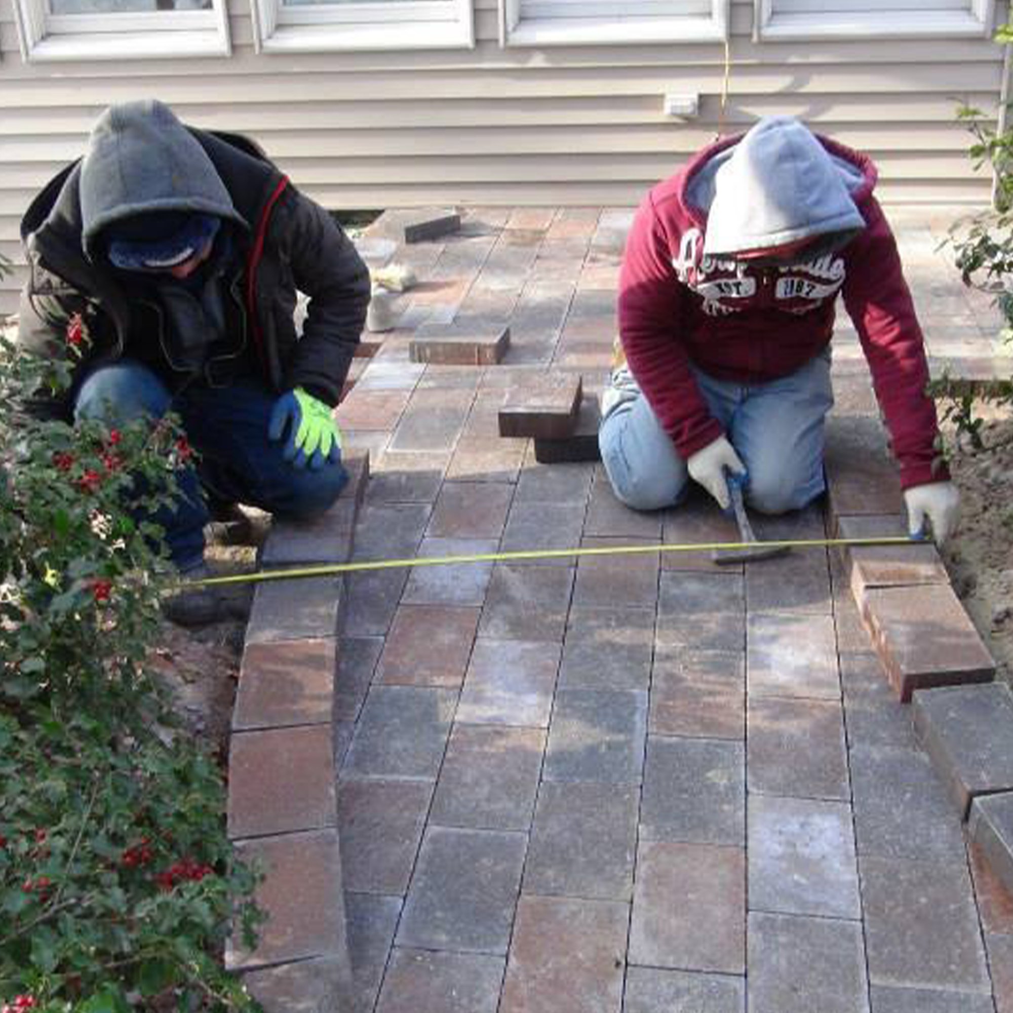 Two people installing stone pavers for a residential walkway that will feature an integrated snow melting system.