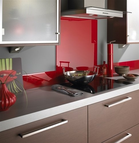 Modern kitchen featuring a glossy red glass backsplash, dark wood cabinetry, and stainless steel cookware on a grey countertop.