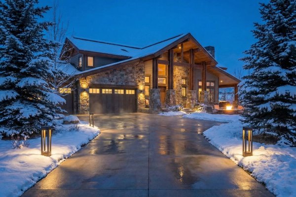 A snow melting system keeps a concrete driveway clear of snow and ice at a rustic-modern home during a winter evening.