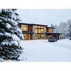 A modern luxury home with a snow melting system clearing the driveway during a winter landscape.