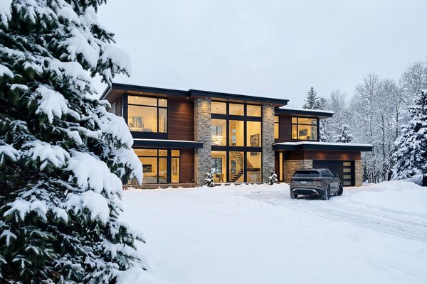 A modern luxury home with a snow melting system clearing the driveway during a winter landscape.