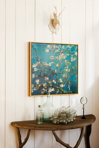 A framed print of Vincent van Gogh's Almond Blossoms hanging above a rustic wooden console table with decorative accents on a white paneled wall.