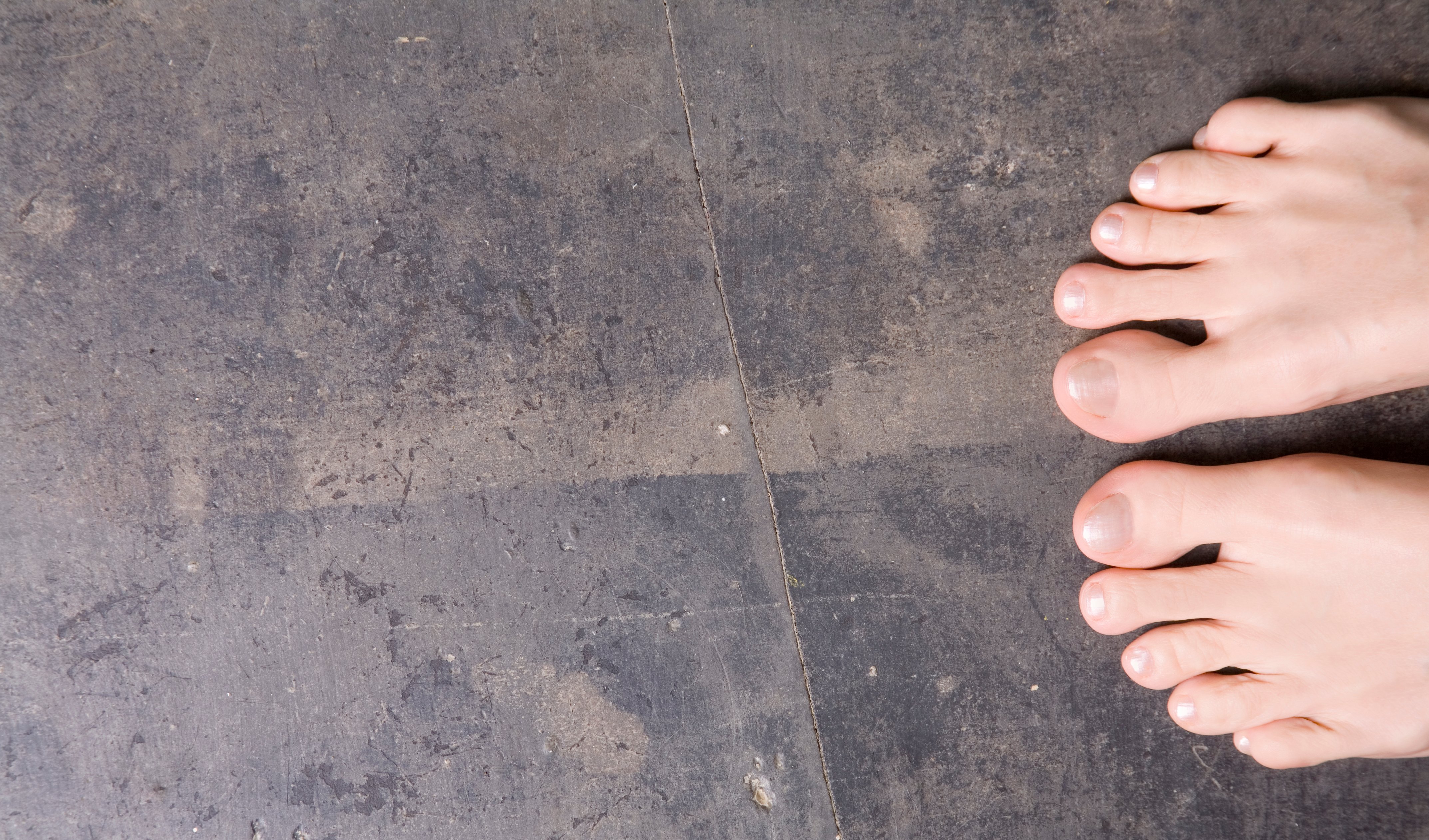 Bare feet standing on a textured, dark distressed concrete floor.