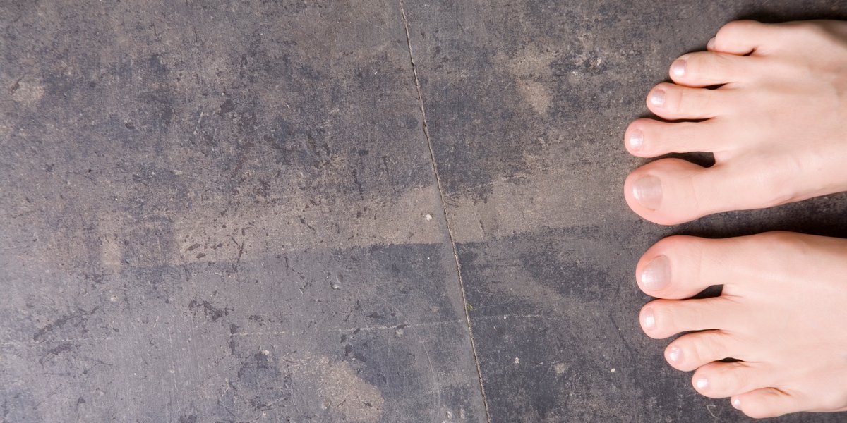 Bare feet standing on a textured, dark distressed concrete floor.
