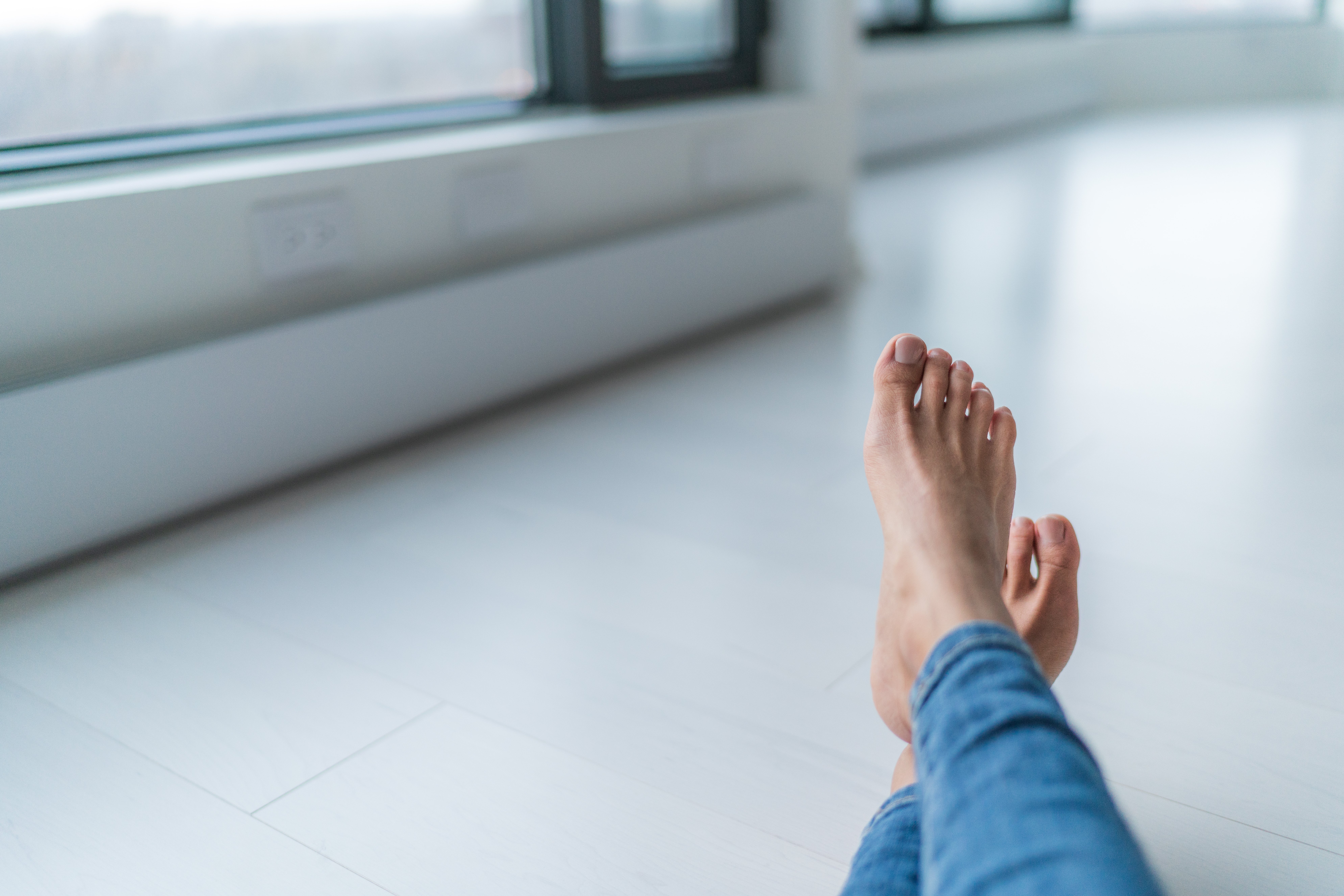 Bare feet resting on a floor with baseboard heating in a brightly lit modern room.