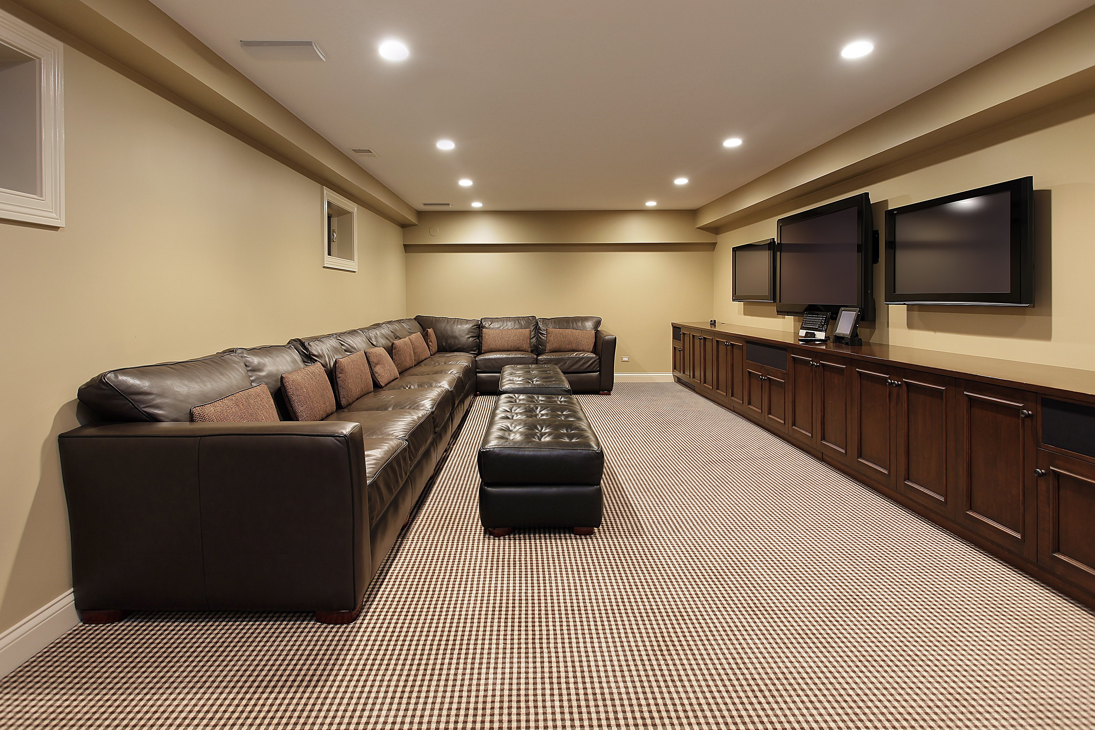 A finished basement media room featuring a leather sectional sofa and media console installed over a carpeted floor.