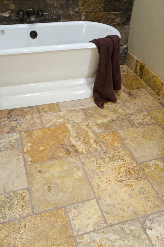 Earth-toned stone tile bathroom floor with a freestanding soaking bathtub and oil-rubbed bronze fixtures.