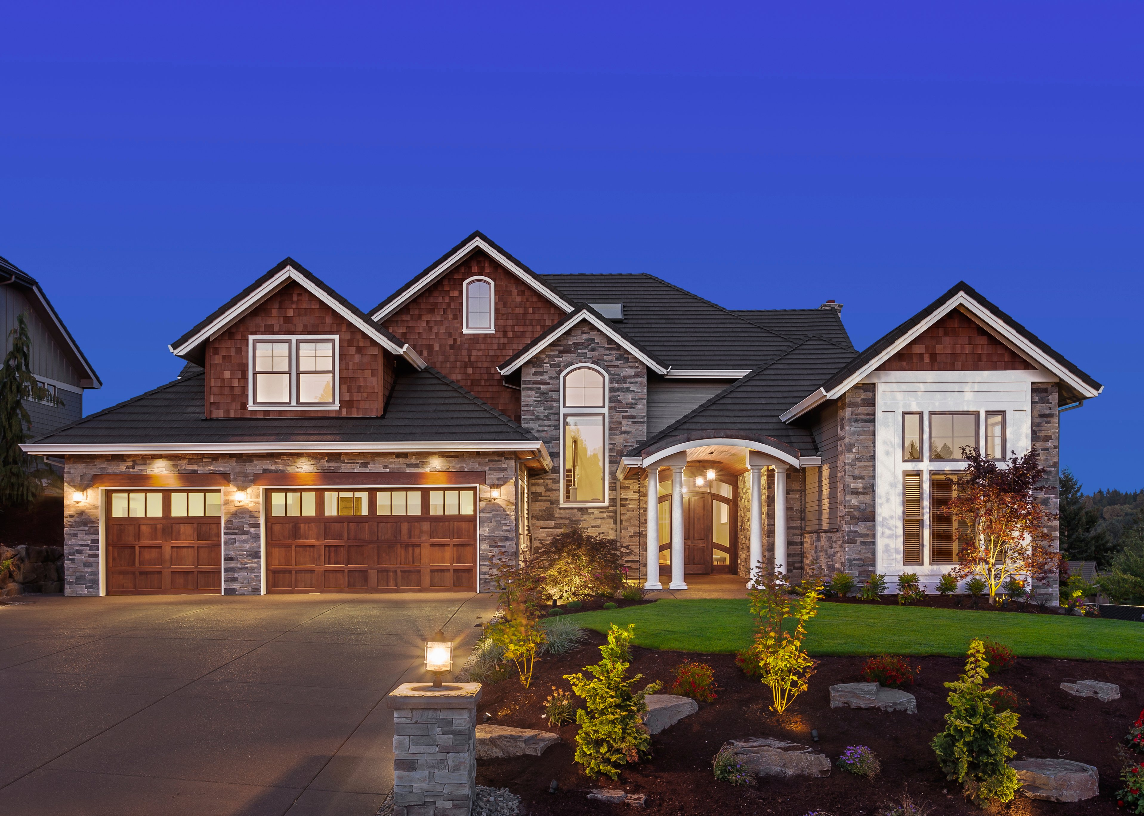 A multi-story craftsman-style house at dusk with an attached garage and a bedroom located directly above the garage space.