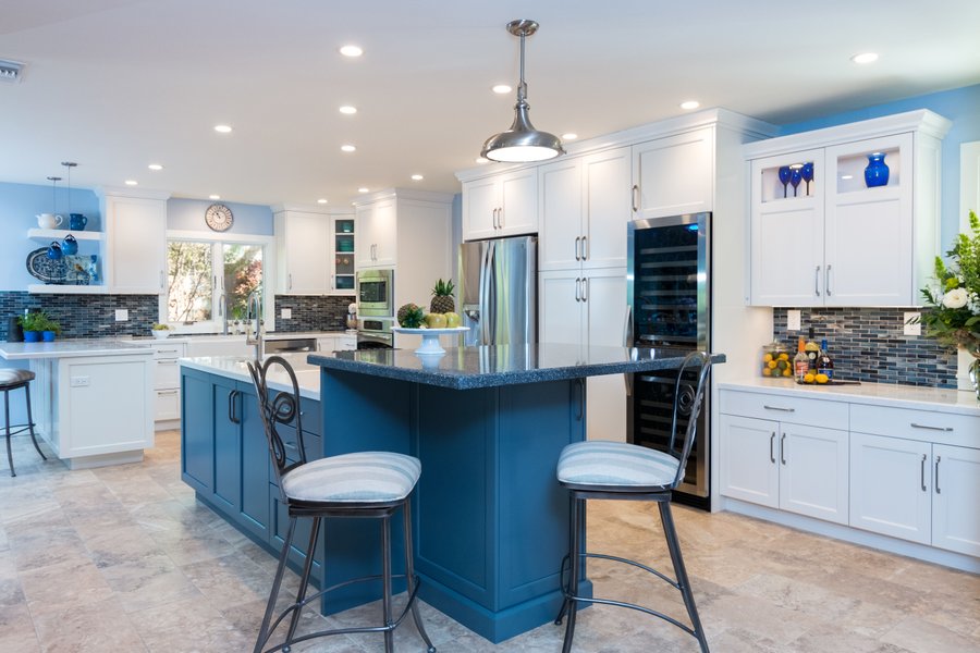 Wide view of kitchen remodel featuring a blue central island and heated stone tile flooring.
