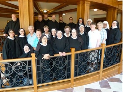 A group of nuns and monks standing on a mezzanine overlooking a finished stone floor with a diamond checkerboard pattern at St. Scholastica Priory.
