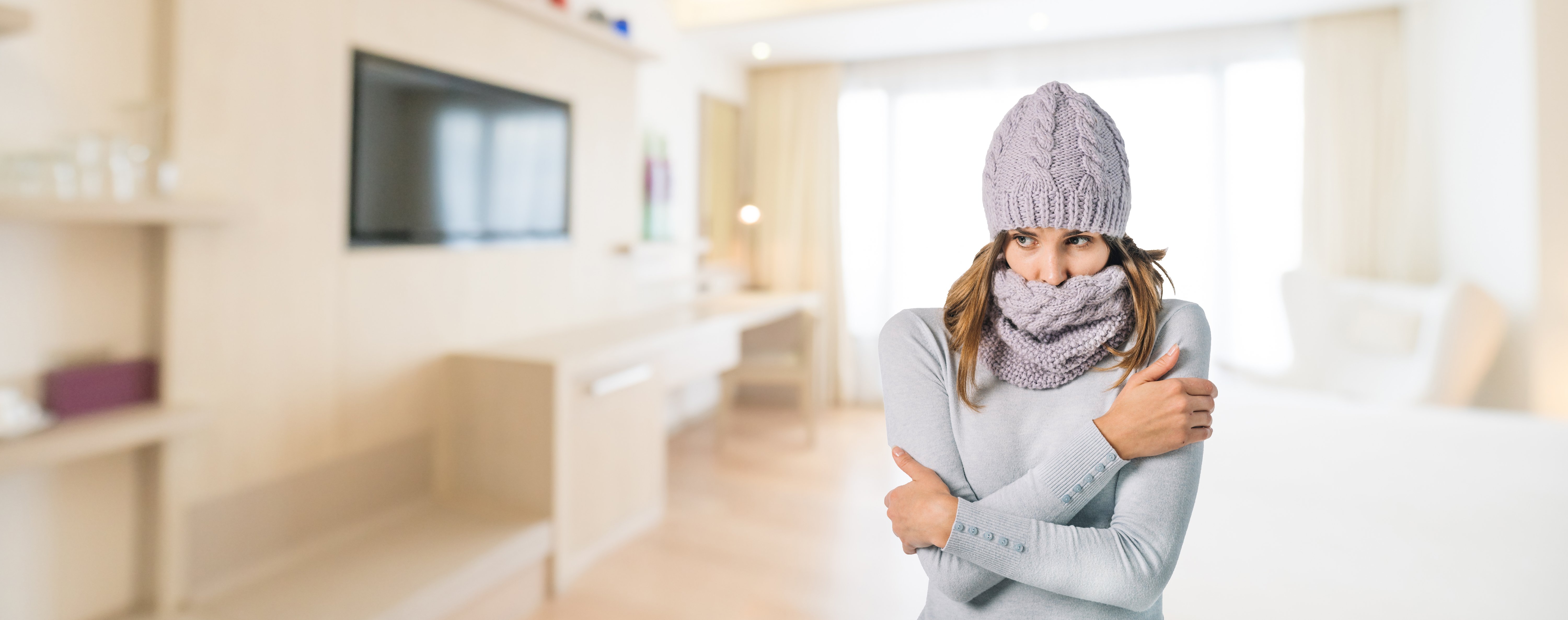 A woman shivering in a cold living room, highlighting the need for electric radiant floor heating to provide comfort in modern home interiors.