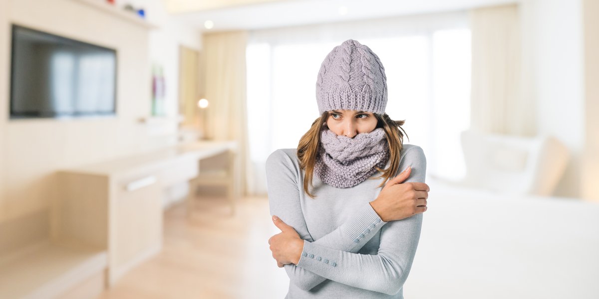 A woman shivering in a cold living room, highlighting the need for electric radiant floor heating to provide comfort in modern home interiors.