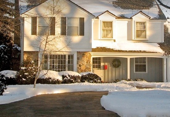 A residential driveway with a snow melting system keeping the asphalt surface clear of snow while surrounding areas remain covered in winter snow.