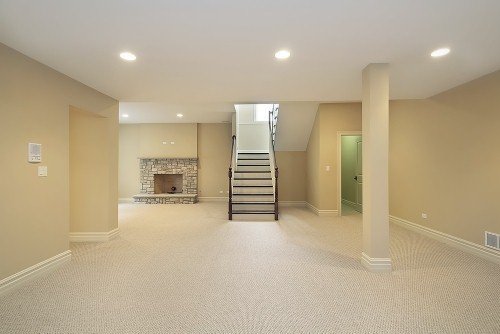 A thermostat mounted on a wall in a finished basement with a stone fireplace and staircase.
