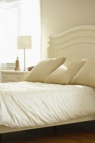 A cozy guest bedroom interior featuring a bed with white linens and a white arched headboard on warm hardwood flooring.