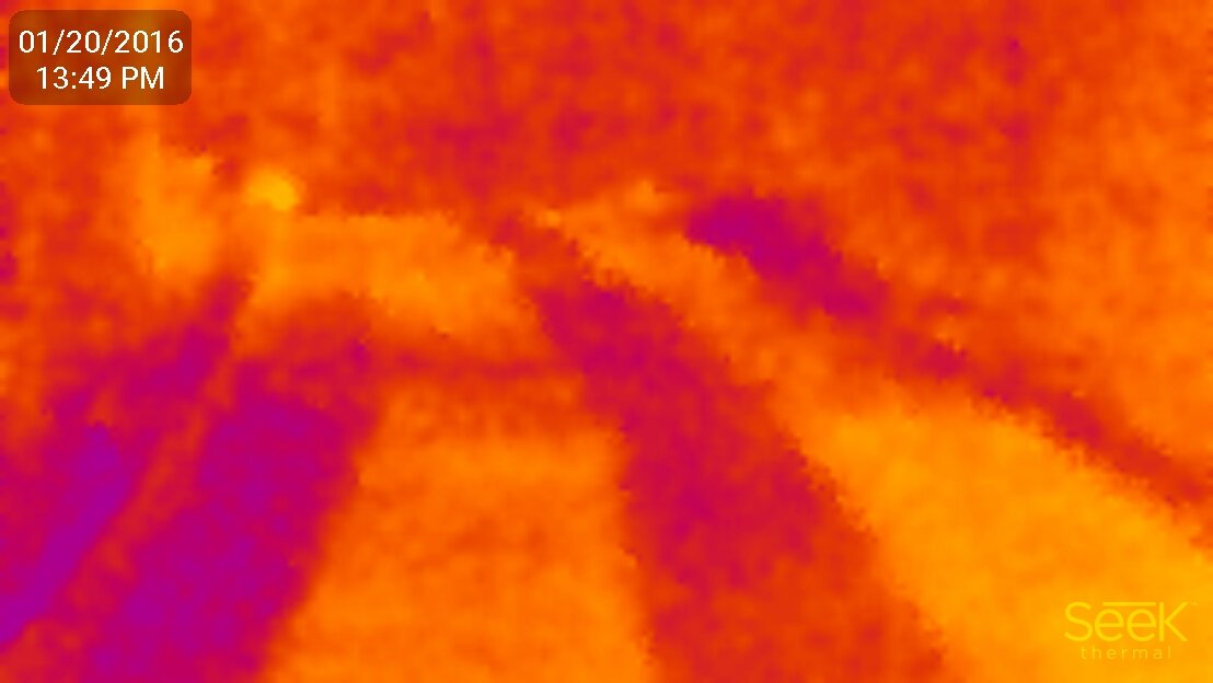 A thermal infrared image of a snow melting heating mat installation, displaying active heat patterns in yellow and orange across the surface.