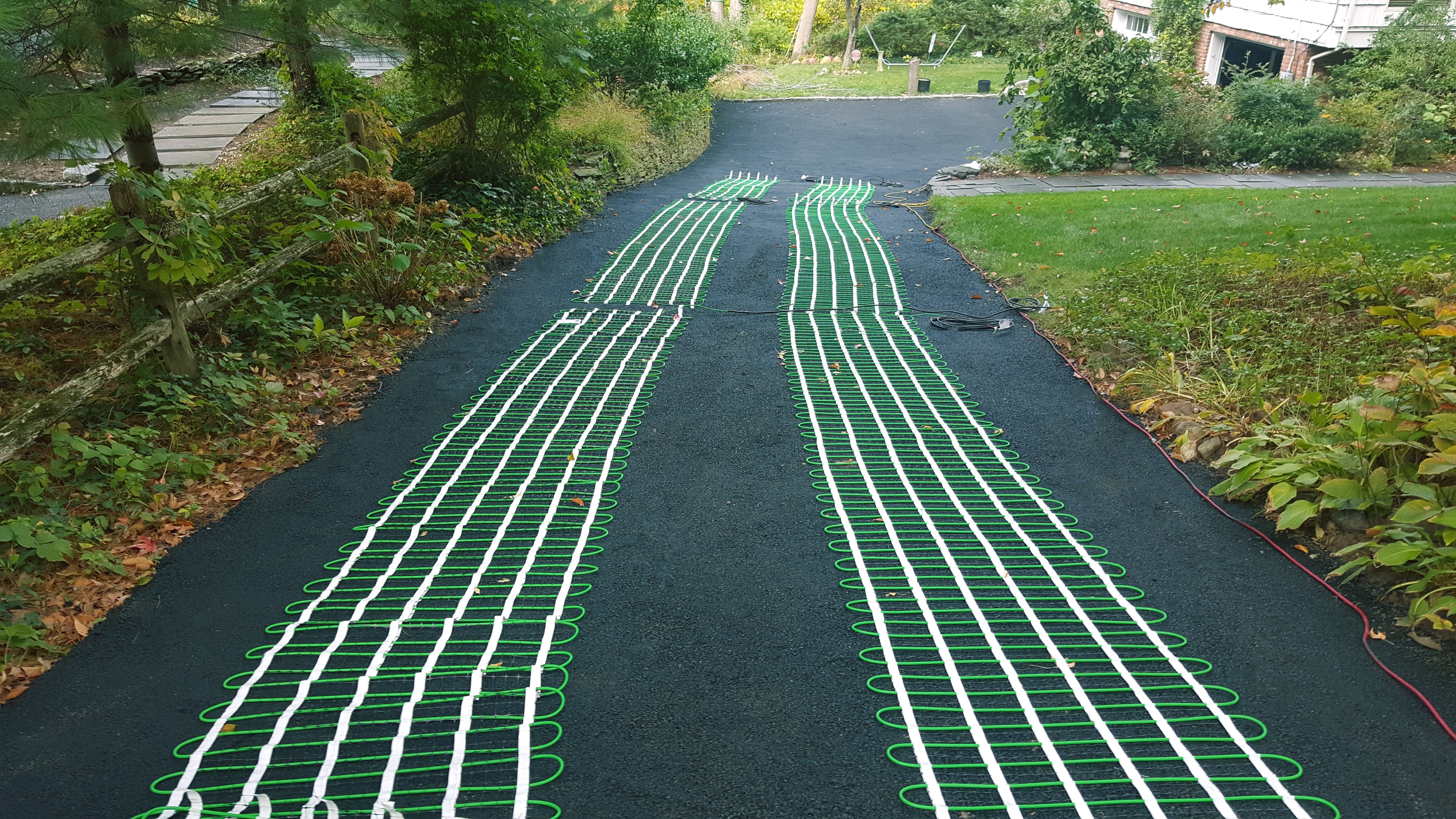 Snow melting heating mats with green cables installed in parallel tracks on an asphalt driveway before the final surface layer.