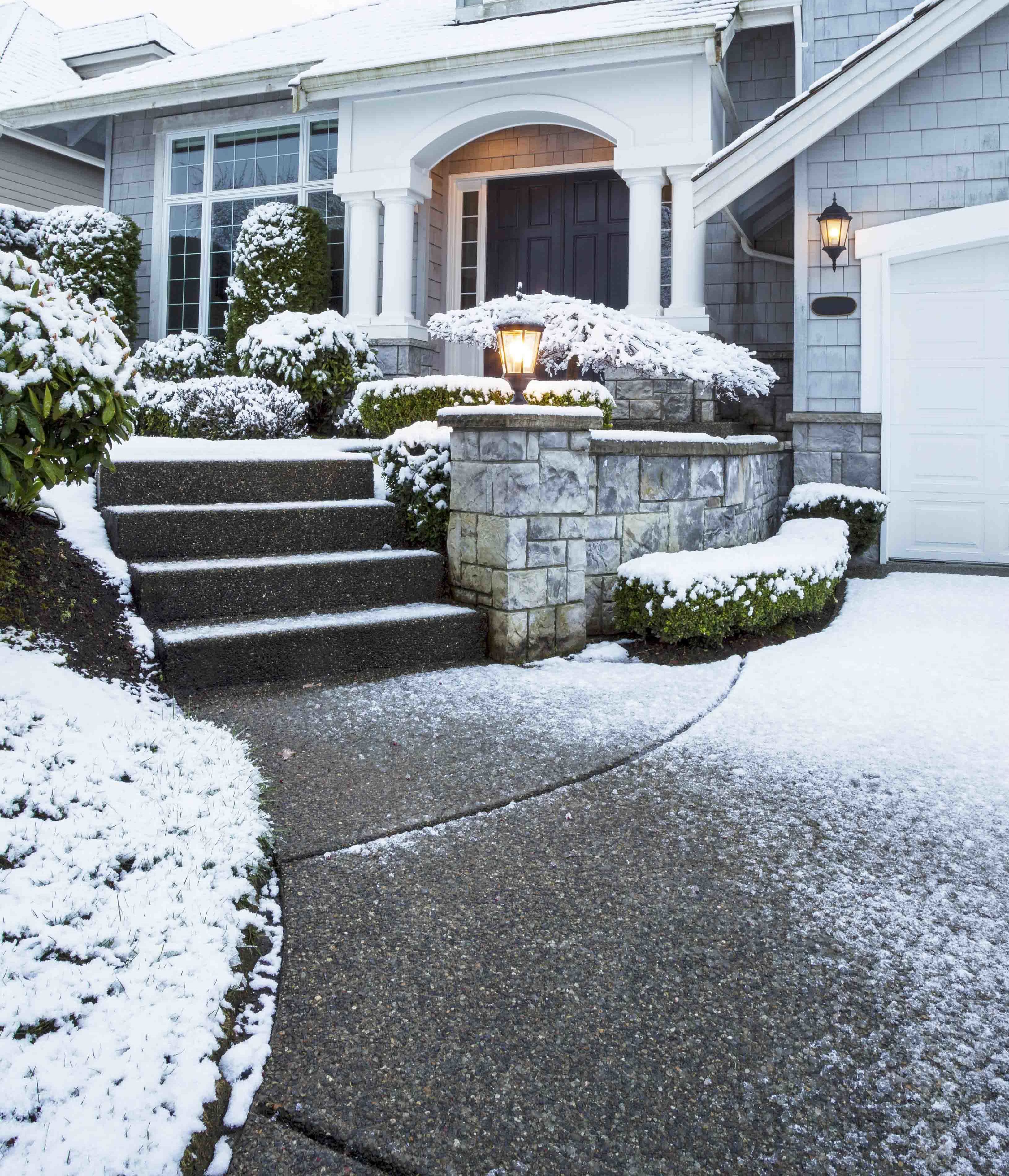 A residential walkway and stairs cleared of snow by a snow melting system, contrasting with the surrounding snow-covered landscape.