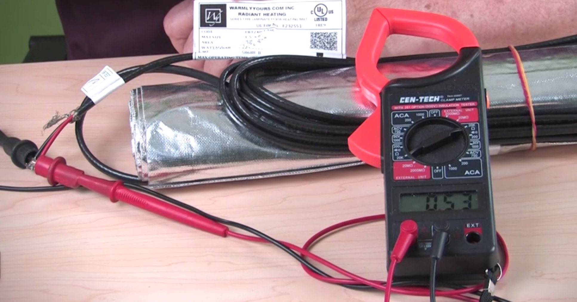 A digital clamp meter testing the resistance of a WarmlyYours Environ electric radiant floor heating mat.