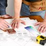 Homeowners and a professional contractor reviewing architectural blueprints and material samples on a wooden table during a home renovation.