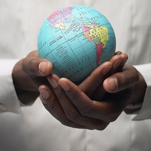A person holding a small desktop political globe featuring South America and the Pacific Ocean to illustrate energy-efficient lifestyle tips.