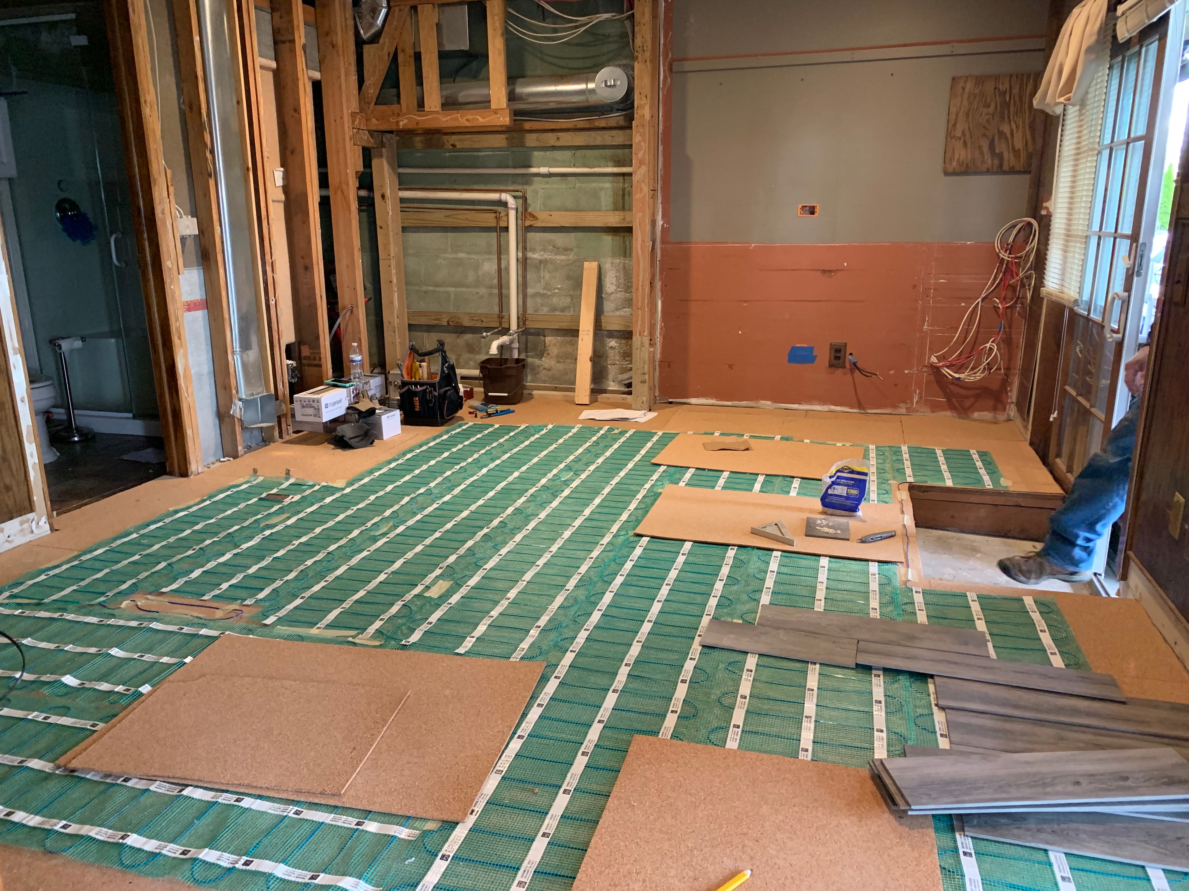 Electric floor heating mats laid over cork underlayment during a basement remodel.