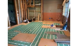 Electric floor heating rolls being installed with cork underlayment in basement remodel