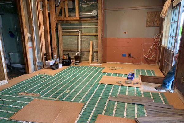 Electric floor heating mats laid over cork underlayment during a basement remodel.