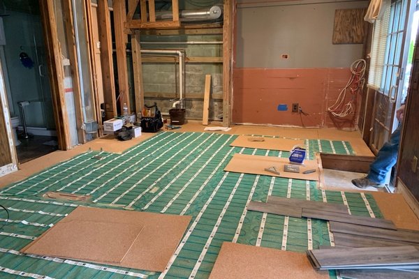 Electric floor heating rolls being installed with cork underlayment in basement remodel