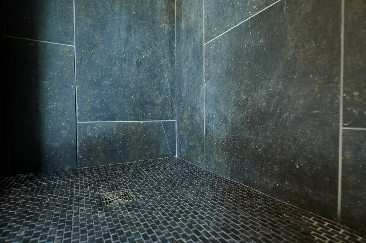 Electric radiant floor heating installed beneath dark mosaic tile in a walk-in shower with charcoal stone-look wall tiles.