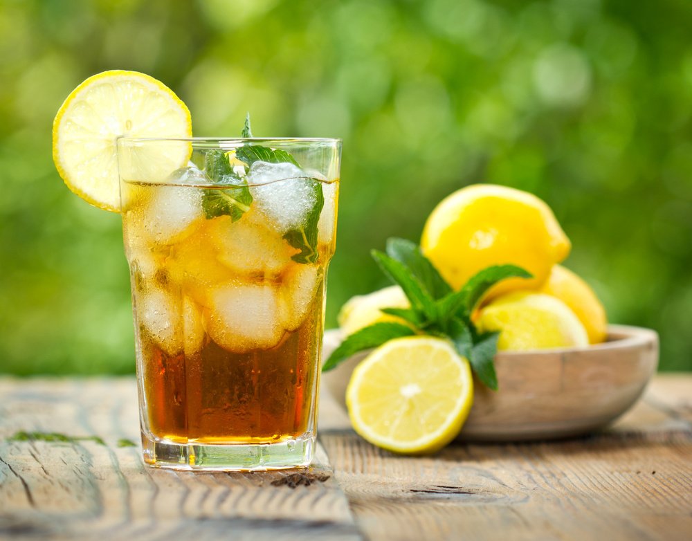A glass of iced tea with lemon and mint on a rustic wooden table in a garden setting.