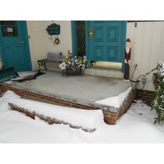 A clear concrete porch landing free of snow during winter, maintained by an installed snow melting system despite surrounding heavy snowfall.