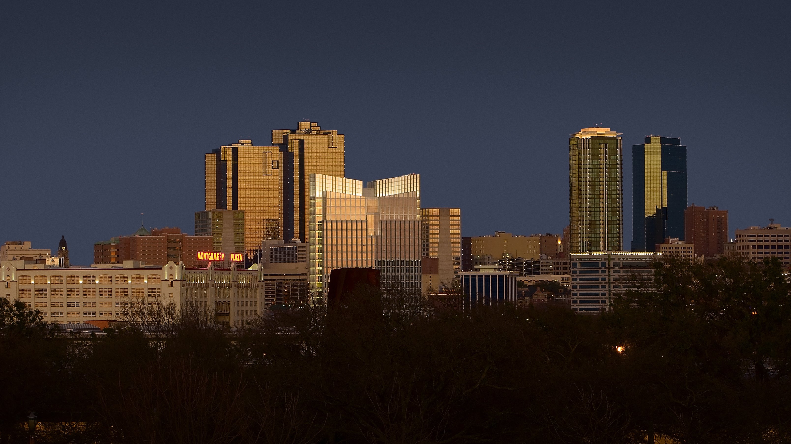 The Montgomery Plaza building illuminated against the Fort Worth city skyline during a twilight sunset.
