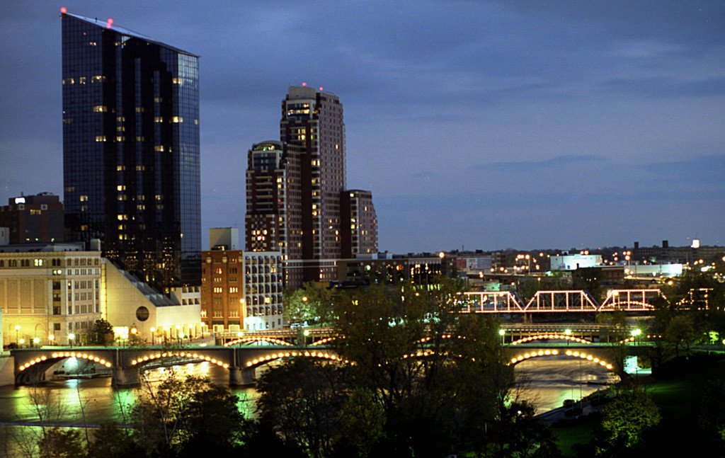 The Grand Rapids, Michigan skyline at night featuring illuminated bridges over the Grand River and the Plaza Towers building.