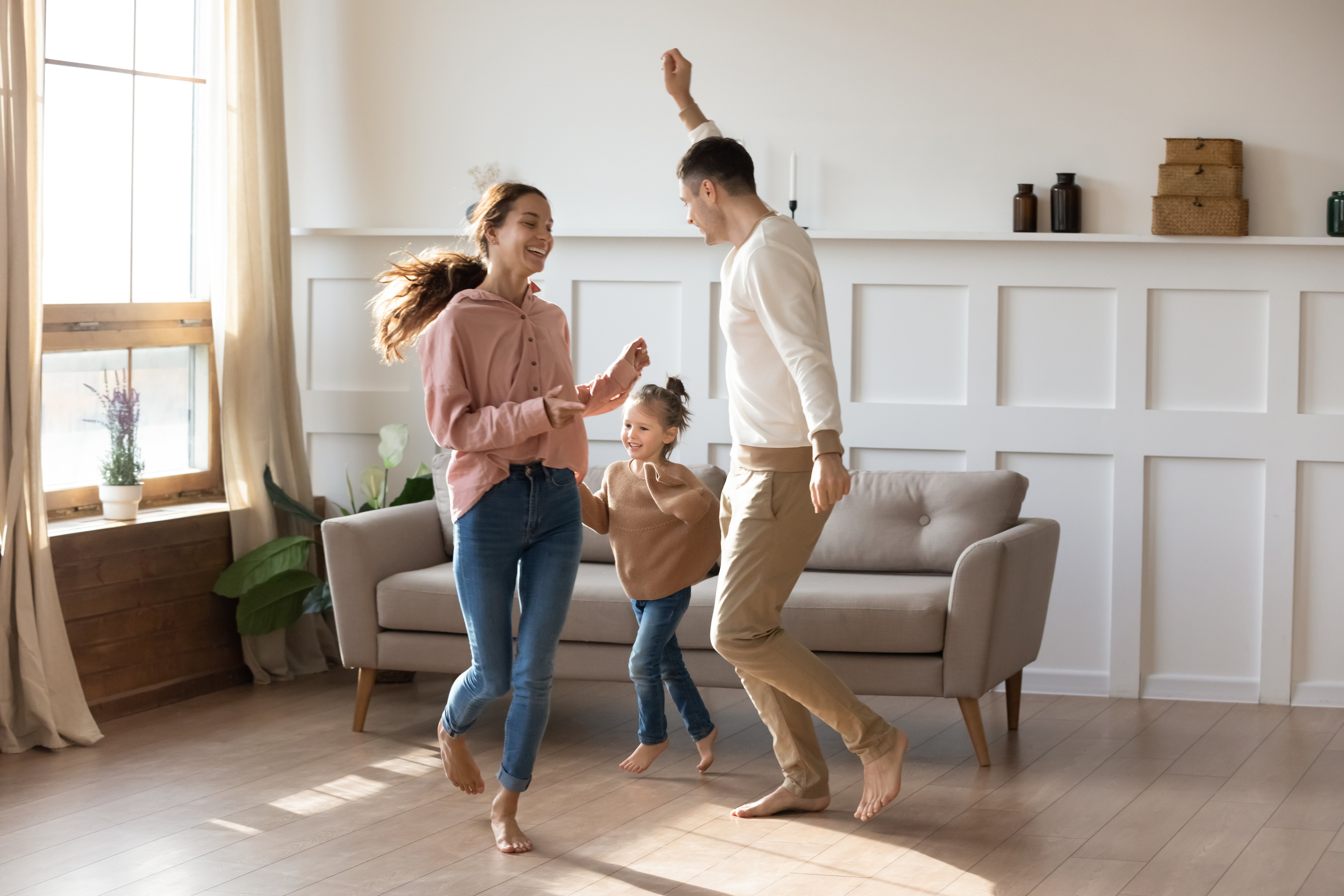 A happy family dancing barefoot on a modern living room floor with electric radiant floor heating.