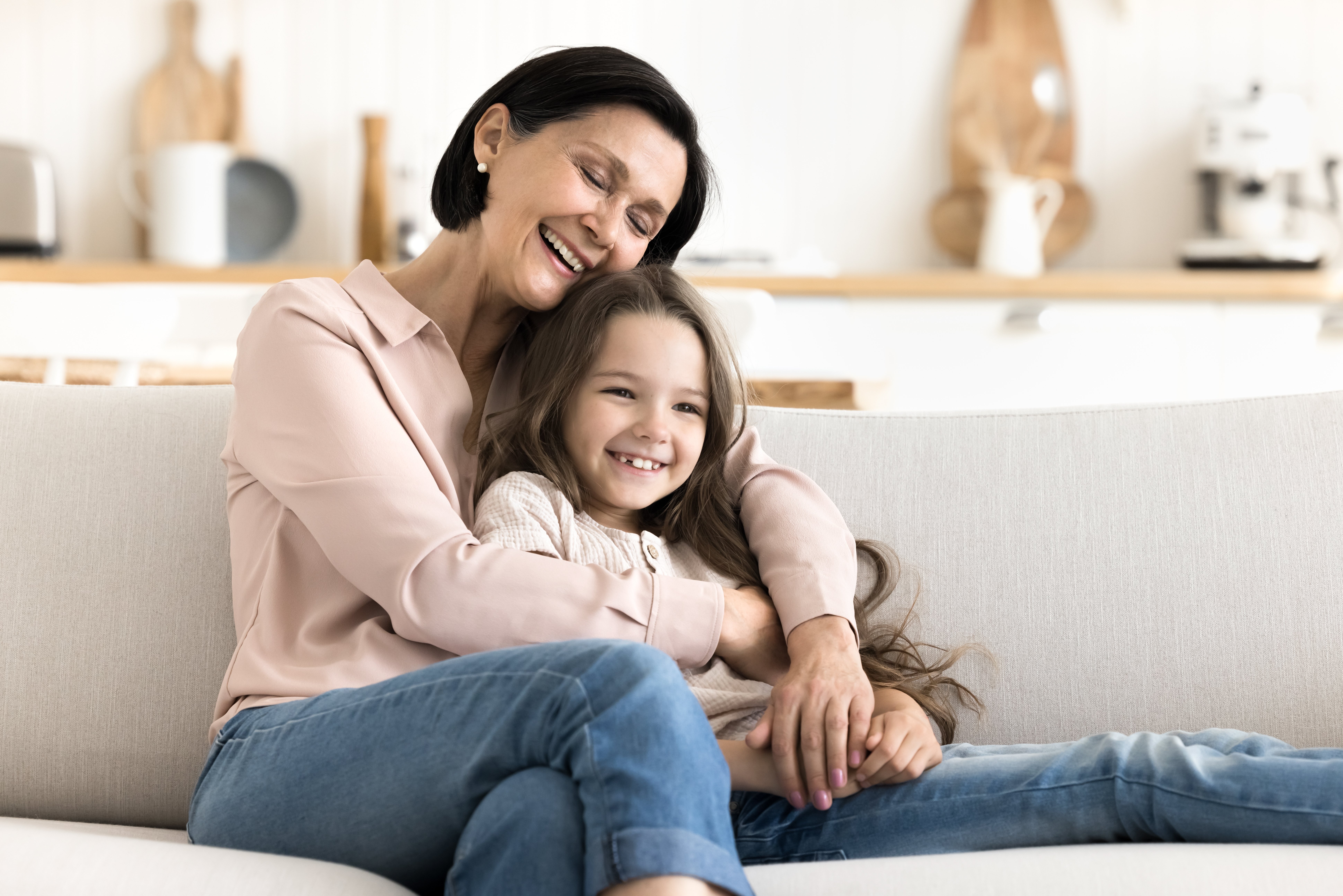 A mother and daughter laughing together while sitting on a sofa in a bright, modern home interior.