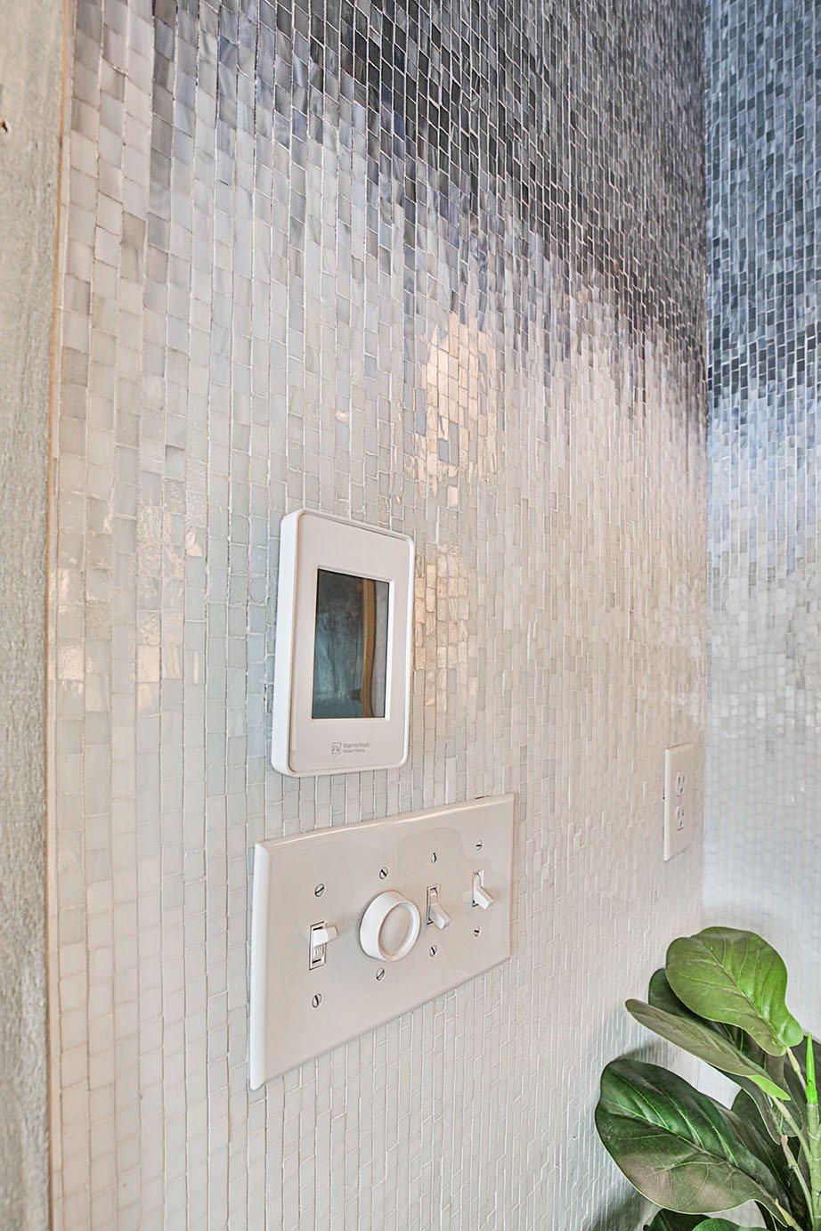 Close-up of WarmlyYours nSpire Touch floor heating thermostat mounted on a light mosaic tile wall.