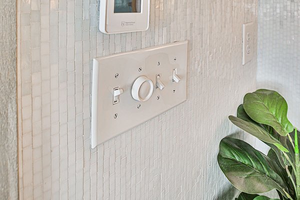 Close-up of WarmlyYours nSpire Touch floor heating thermostat mounted on a light mosaic tile wall.