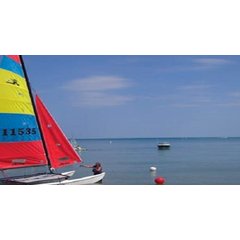 A small catamaran sailboat with colorful sails anchored in the calm waters of the Highland Park lakefront.