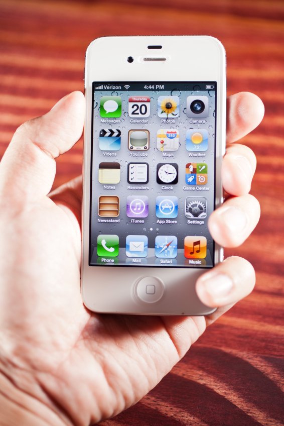 A hand holding an iPhone displaying home improvement apps over a wood grain surface.