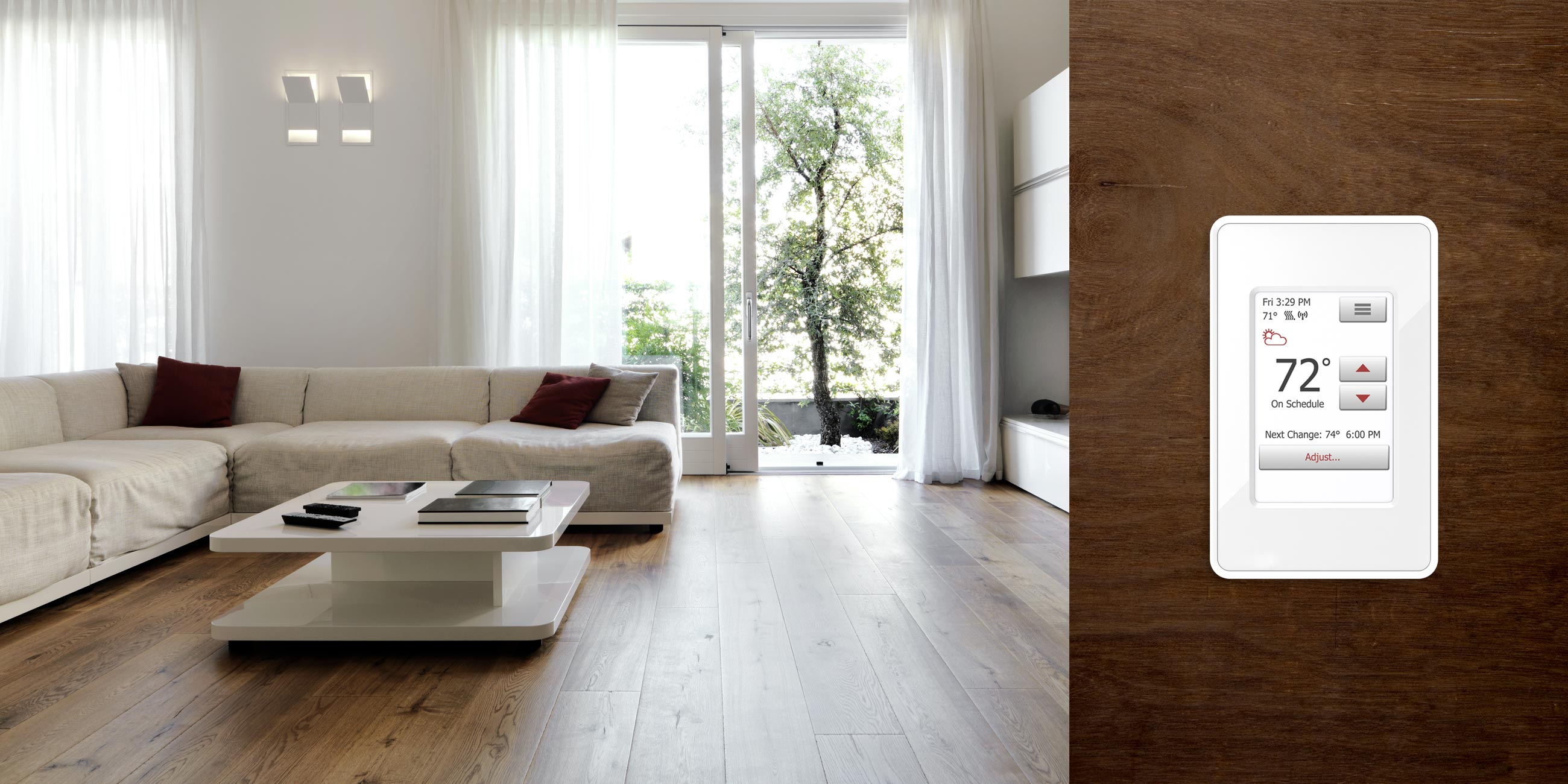 An nSpire Touch WiFi programmable thermostat mounted on a dark wood panel next to a bright living room with light wood flooring.