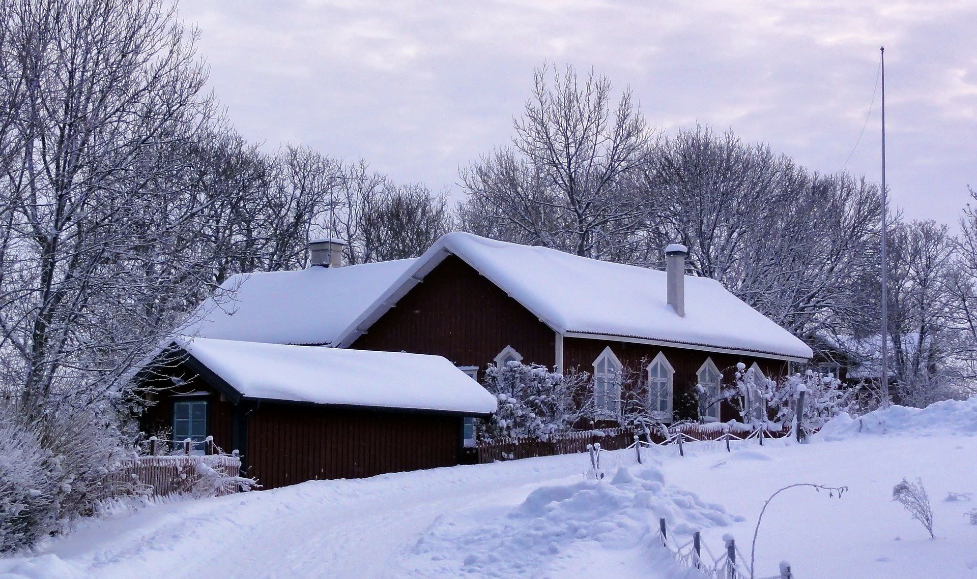 A traditional wooden house and driveway covered in heavy snow during a winter landscape scene.