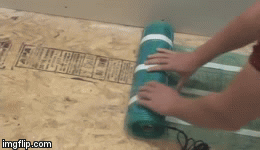 A TempZone Flex Roll electric radiant floor heating mat with blue heating cables on green mesh being unrolled across a subfloor.