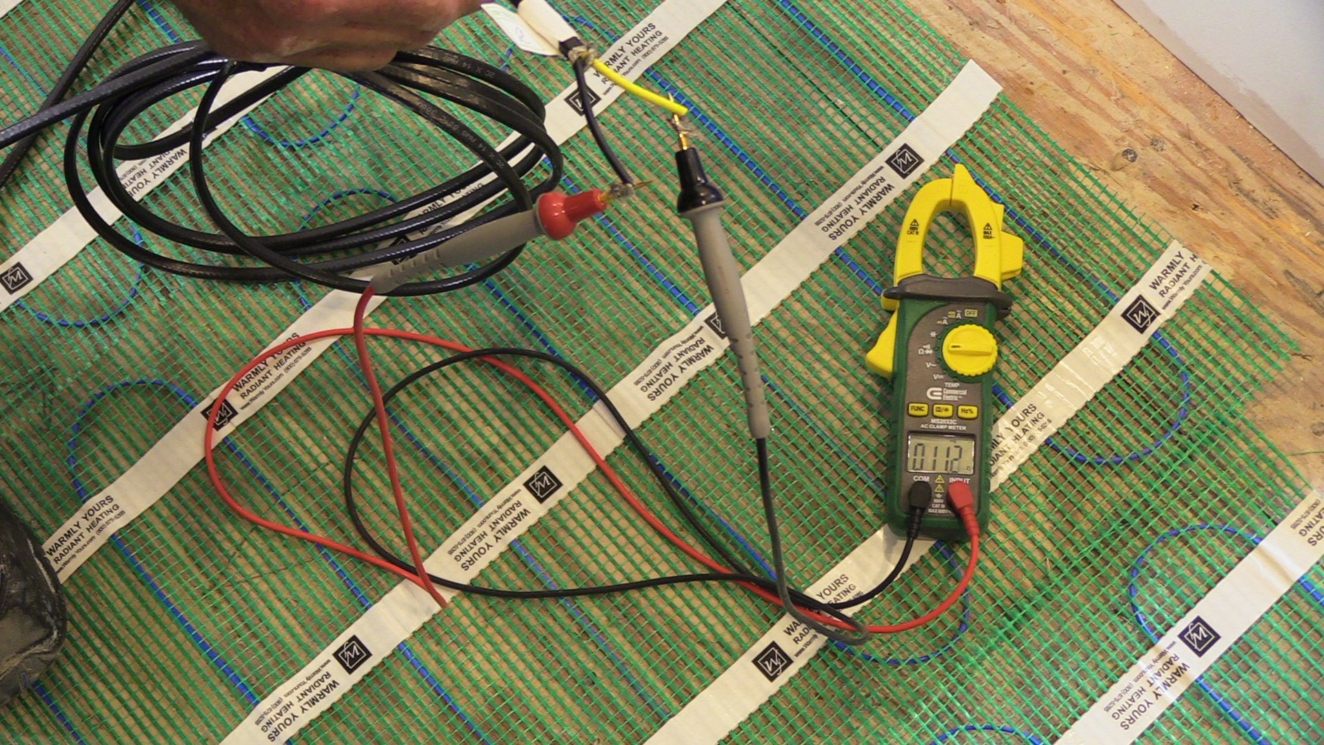 A digital ohmmeter testing the electrical continuity of radiant floor heating cables before installation.