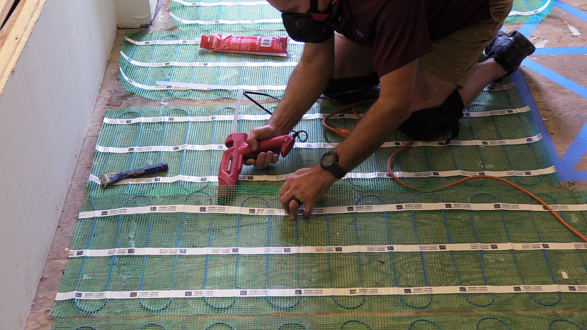 Installing a TempZone™ heating mat with a hot glue gun to fasten it to the subfloor during floor heating layout.