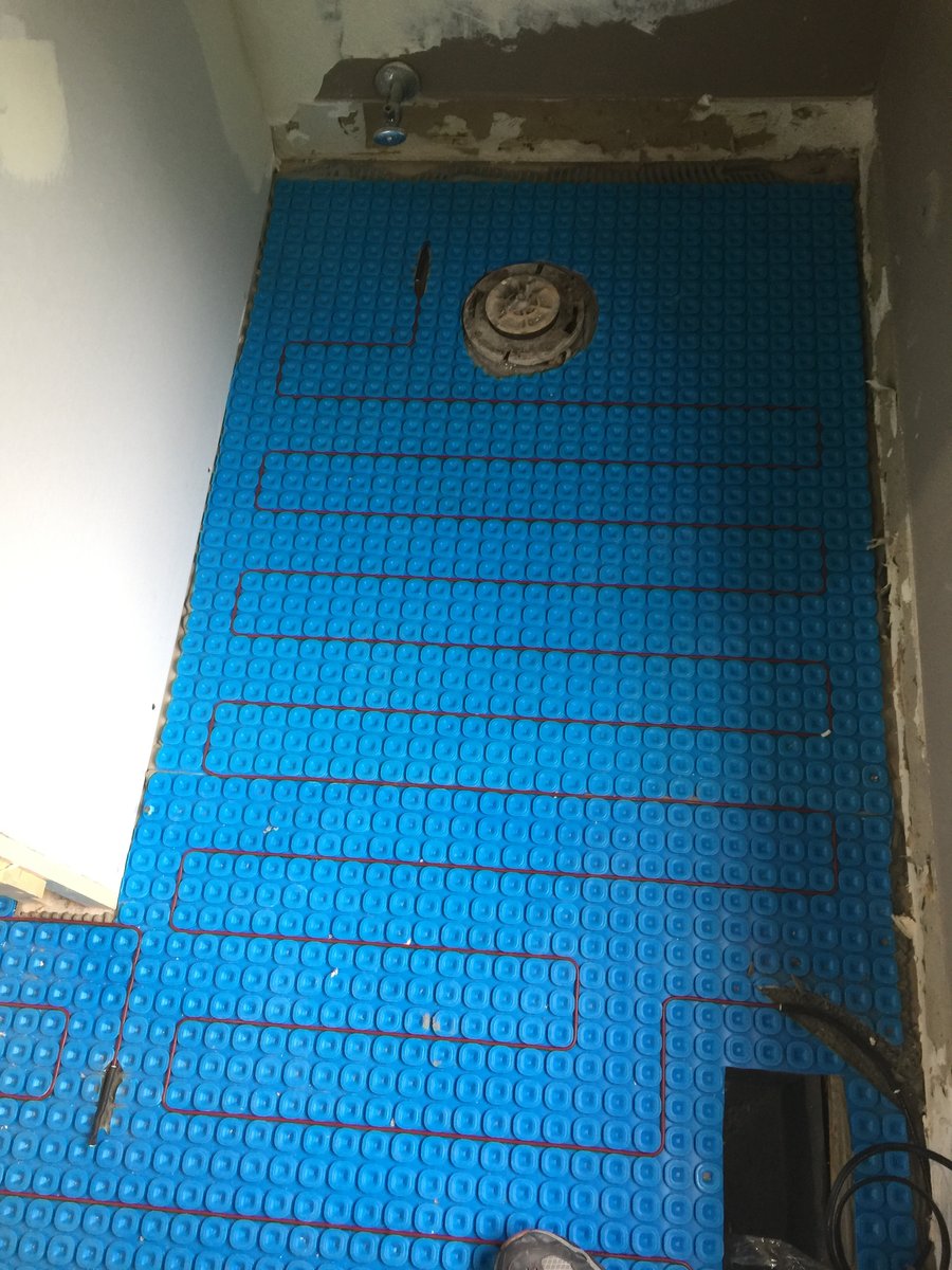 Electric floor heating cable woven into a blue Prodeso uncoupling membrane around a bathroom fixture.