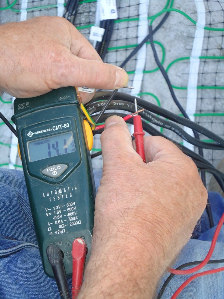 A technician testing the electrical resistance of a snow melting heating mat with a Greenlee multimeter before installation on a concrete base.