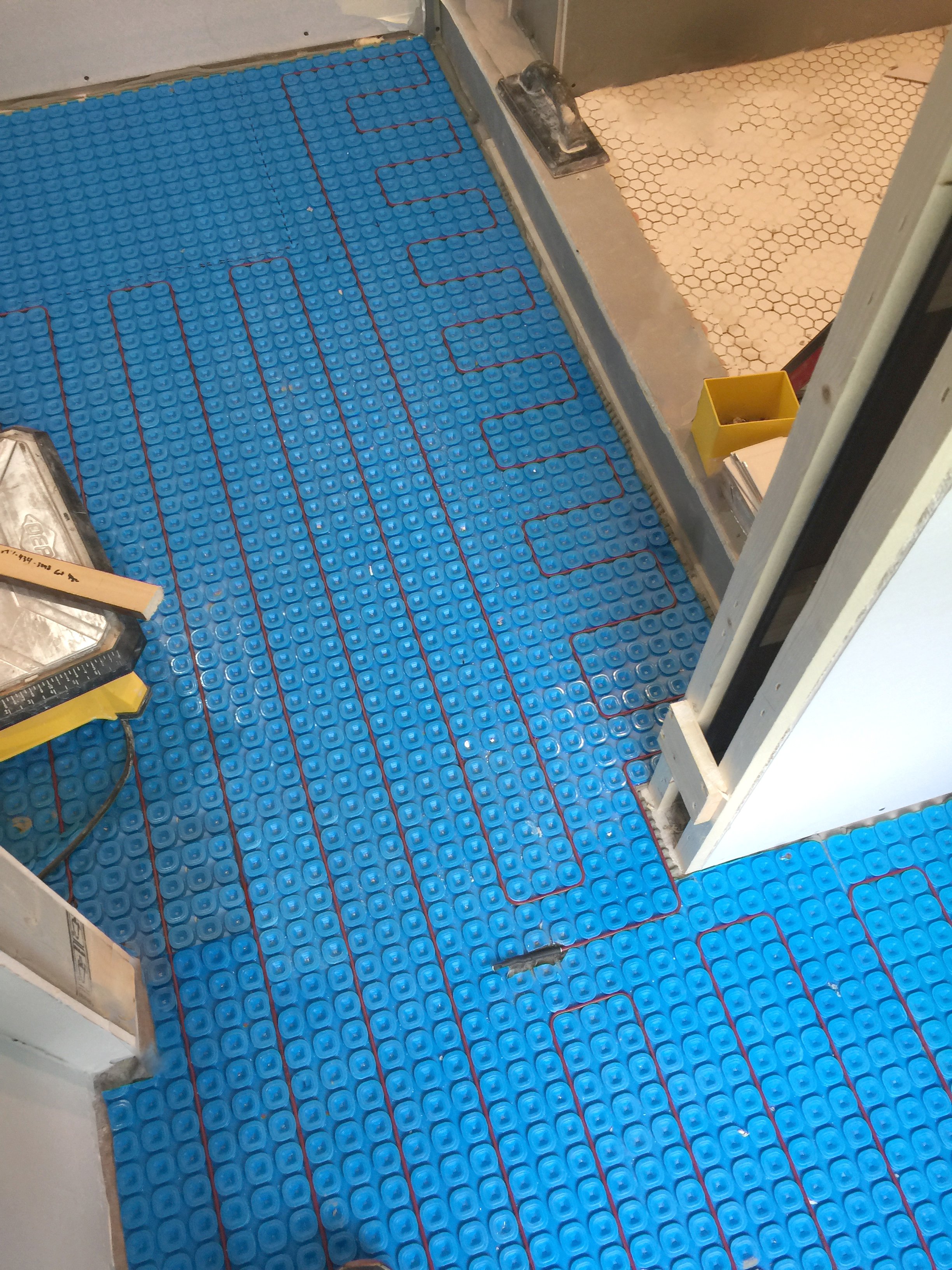 Floor heating sensor probe embedded between electric heating cables inside a blue uncoupling membrane.